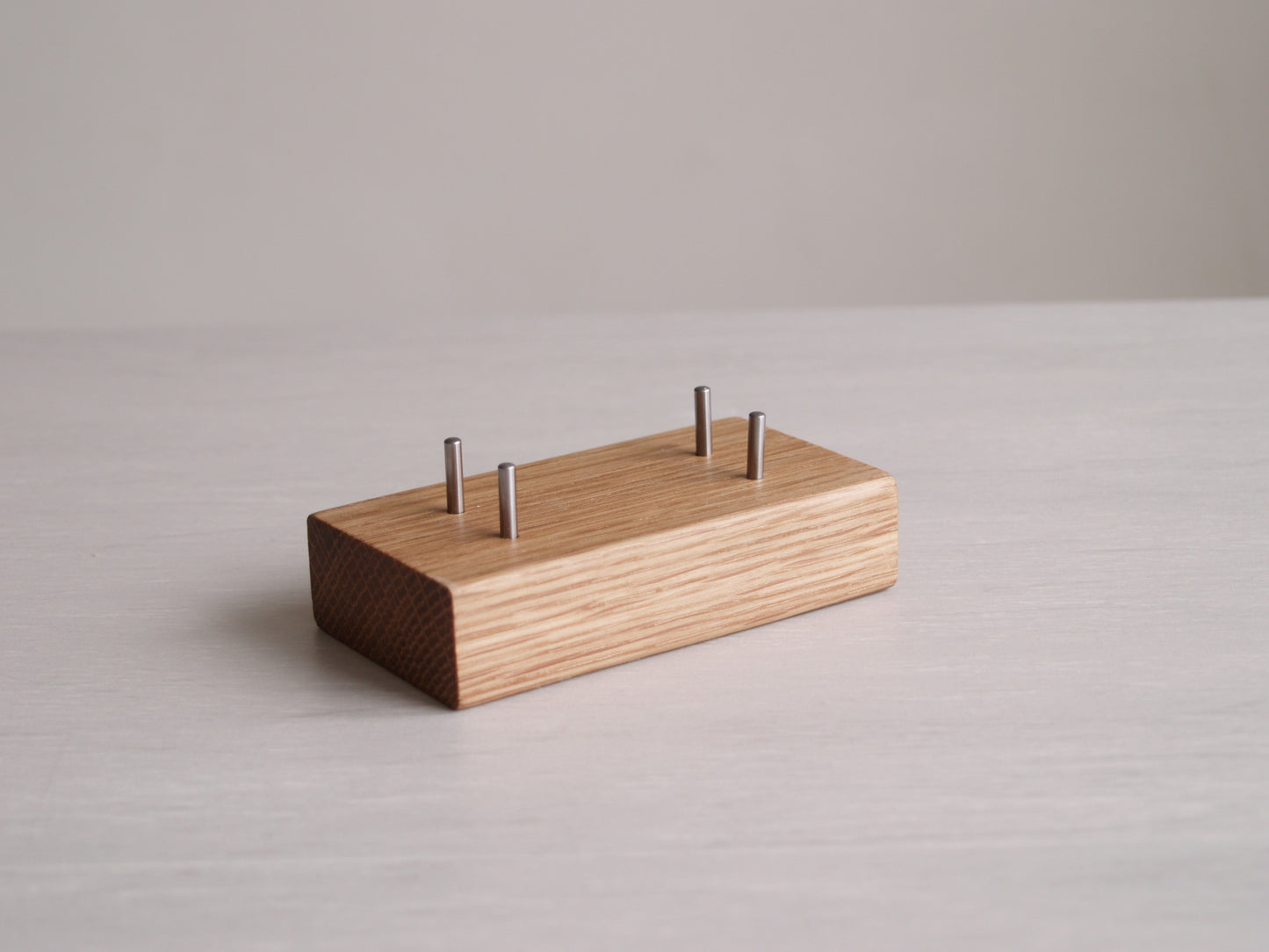 A small block of solid oak with four stainless steel pins, used for holding business cards.