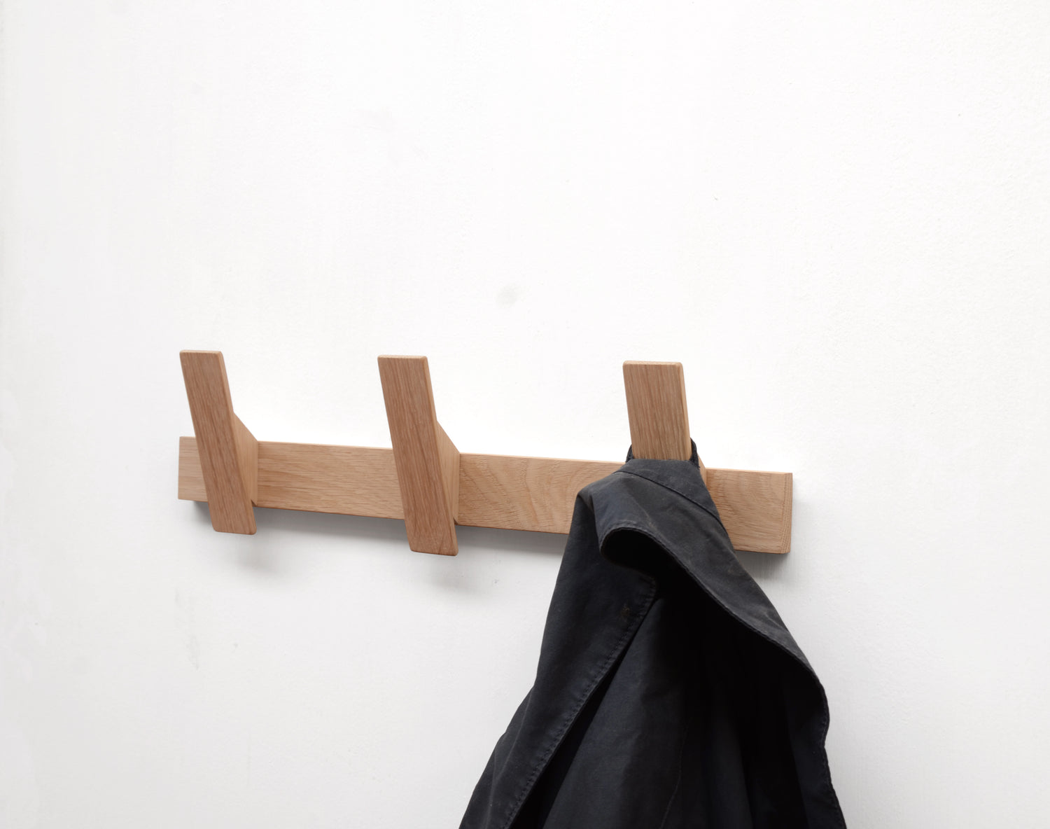 Solid oak coat rack with three hooks and blue coat. Minimalist, contemporary style.